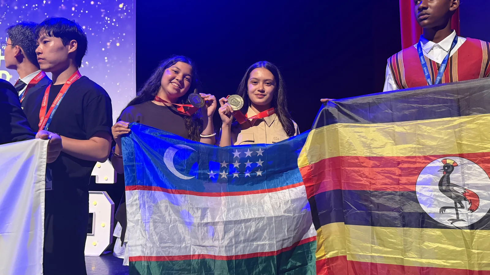 Two CST students holding gold medals and the flag of Uzbekistan