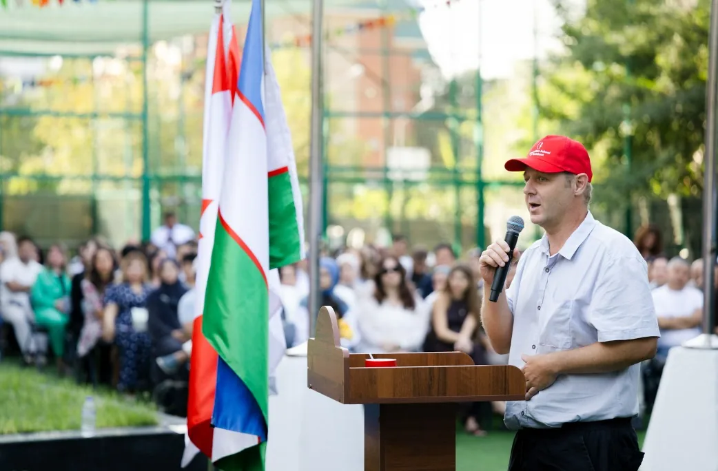 A member of CST staff addressing the assembly from the podium, beside the flag of Uzbekistan